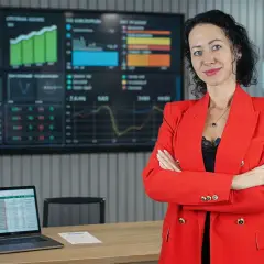 Kobieta w czerwonej marynarce stoi przed ekranem z wykresami. W tle neon "Cit w Praktyce". Może to być związane z tematem paypo zwrot towaru.