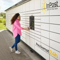 Kobieta z telefonem przy Paczkomacie InPost. Szybka wysyłka InPost za granicę to teraz norma.