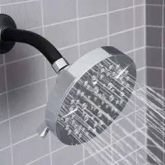 Chromowana deszczownica z czarnym ramieniem, z której leci woda, na tle szarej, kwadratowej mozaiki.