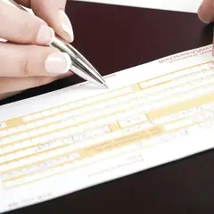 Dłoń z długopisem wypełnia formularz przelewu tradycyjnego.
