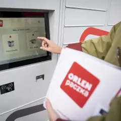 Kobieta z paczką ORLEN Paczka dotyka ekranu automatu, by nadać przesyłkę.