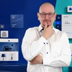Mężczyzna w okularach zastanawia się nad danymi e-commerce. Widoczne są wykresy sprzedaży, zamówień i klientów, a także produkty. Paypo weryfikacja jest kluczowa dla analizy.