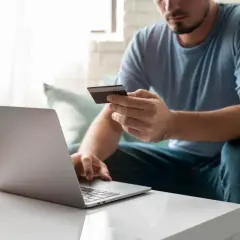 Mężczyzna z kartą kredytową przed laptopem, przygotowuje się, jak wpłacić pieniądze na PayPal.
