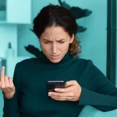 Zmarszczona kobieta trzyma kartę i telefon, zastanawiając się nad bezpieczne zakupy w internecie.
