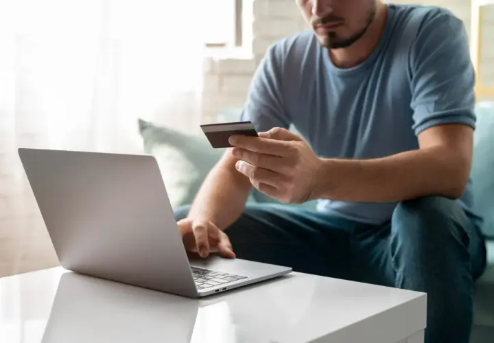 Mężczyzna z kartą płatniczą przed laptopem, uczy się, jak przelać pieniądze na PayPal z konta bankowego.