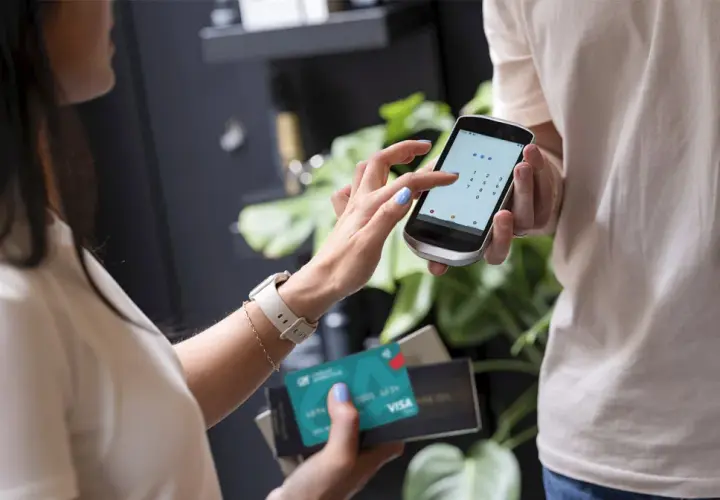 Kobieta wpisuje kod PIN na telefonie, trzymając kartę Visa. Czy płatność kartą w internecie jest bezpieczna? Tak, dzięki nowoczesnym zabezpieczeniom.