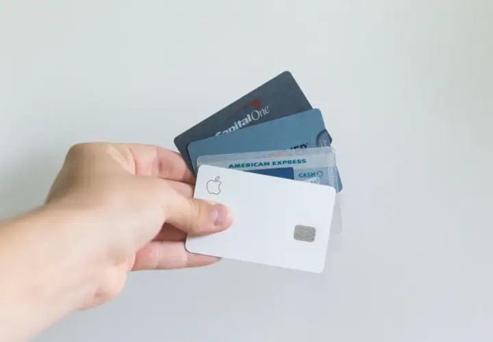 Dłoń trzyma kilka kart płatniczych, w tym białą kartę Apple i kartę American Express.