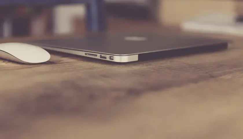 Elegancki, zamknięty laptop biznesowy i biała myszka na drewnianym biurku. Idealny zestaw do pracy.