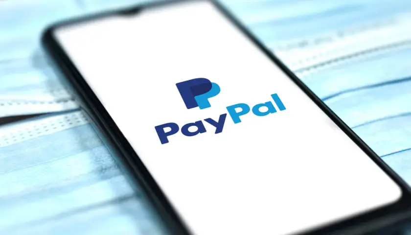 Smartfon z logo PayPal na ekranie, leżący na niebieskich maseczkach ochronnych. Szybkie i bezpieczne płatności online.