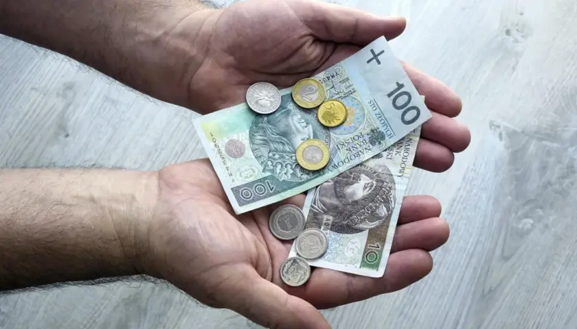 Dłonie trzymają polskie banknoty i monety. To pokazuje, co można sprzedawać w lombardzie, gdy potrzebne są szybkie pieniądze.