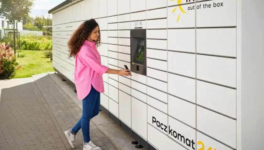 Kobieta z telefonem przy Paczkomacie InPost. Szybka wysyłka InPost za granicę to teraz norma.