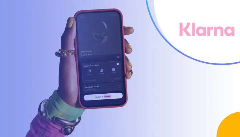 Dłoń trzyma smartfon z aplikacją Klarna, umożliwiającą zakup słuchawek na raty.