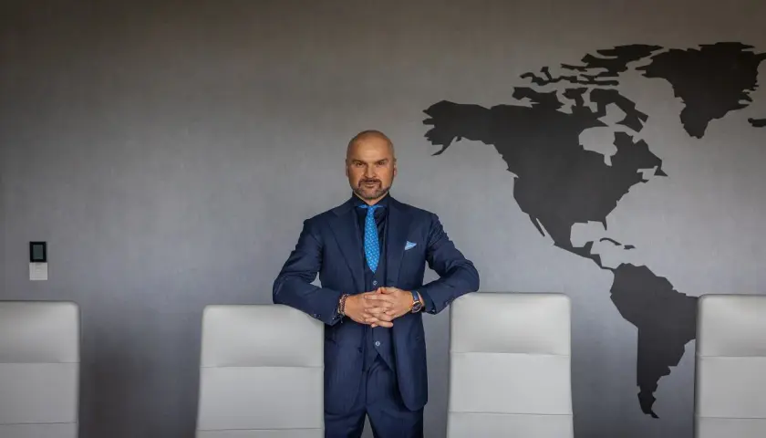 Mężczyzna w garniturze, który stoi przed mapą świata, może być tym, kto wymyślił paczkomaty.