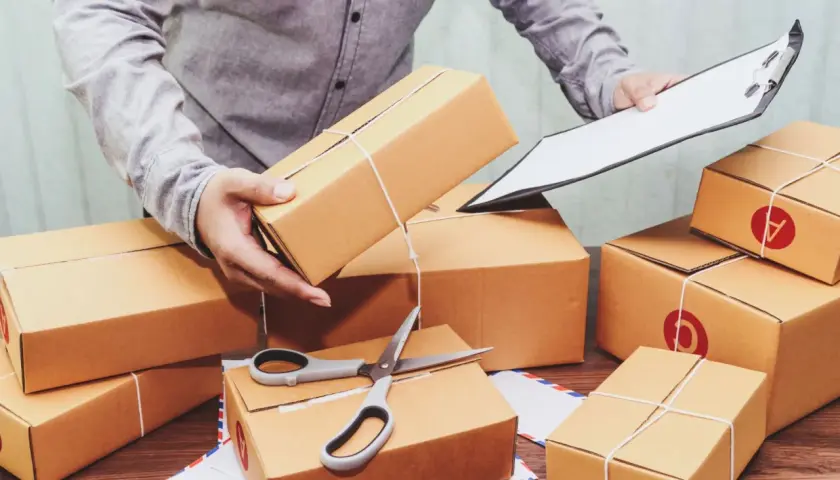Przygotowanie paczek do wysyłki InPost za pobraniem, kiedy pieniądze czekają na odbiór. W tle stosy kartonów, nożyczki i dokumenty.