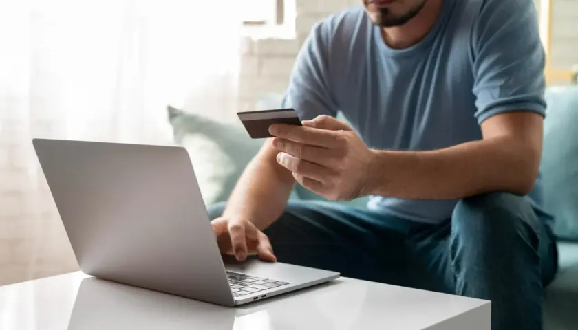 Mężczyzna z kartą płatniczą przed laptopem, uczy się, jak przelać pieniądze na PayPal z konta bankowego.