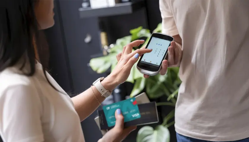 Kobieta wpisuje kod PIN na telefonie, trzymając kartę Visa. Czy płatność kartą w internecie jest bezpieczna? Tak, dzięki nowoczesnym zabezpieczeniom.