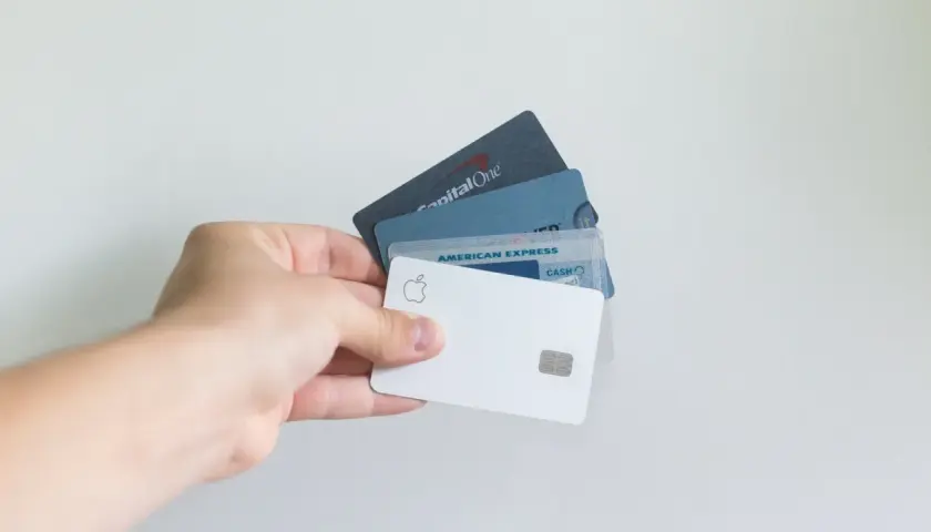 Dłoń trzyma kilka kart płatniczych, w tym białą kartę Apple i kartę American Express.