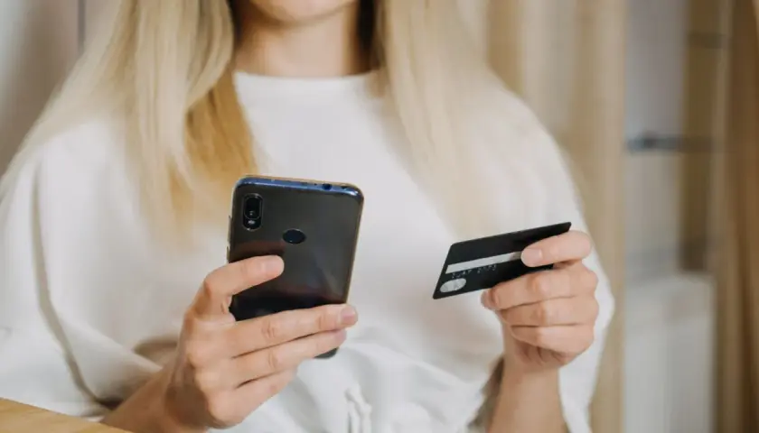 Kobieta z blond włosami trzyma telefon i kartę płatniczą, szukając informacji, jak zwiekszyc limit PayPo.