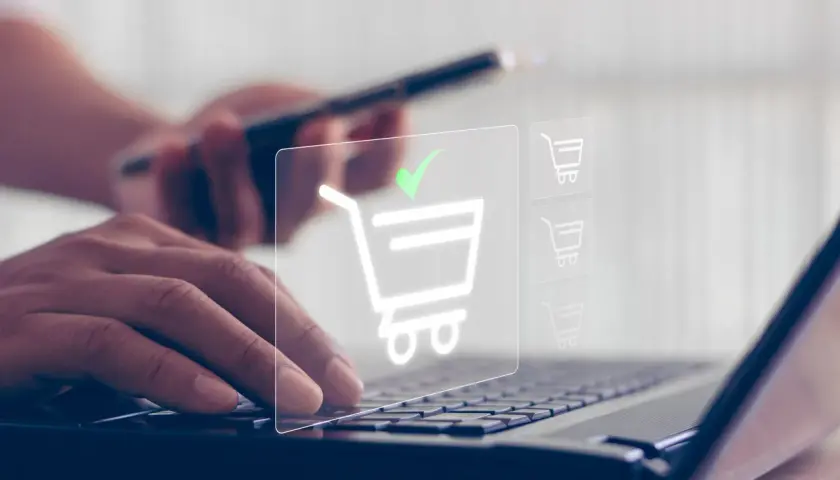 Dłonie wpisują dane na klawiaturze laptopa, a na ekranie pojawia się ikona koszyka z zielonym znacznikiem, symbolizująca udany zakup, jakby płatność przez paysafecard.