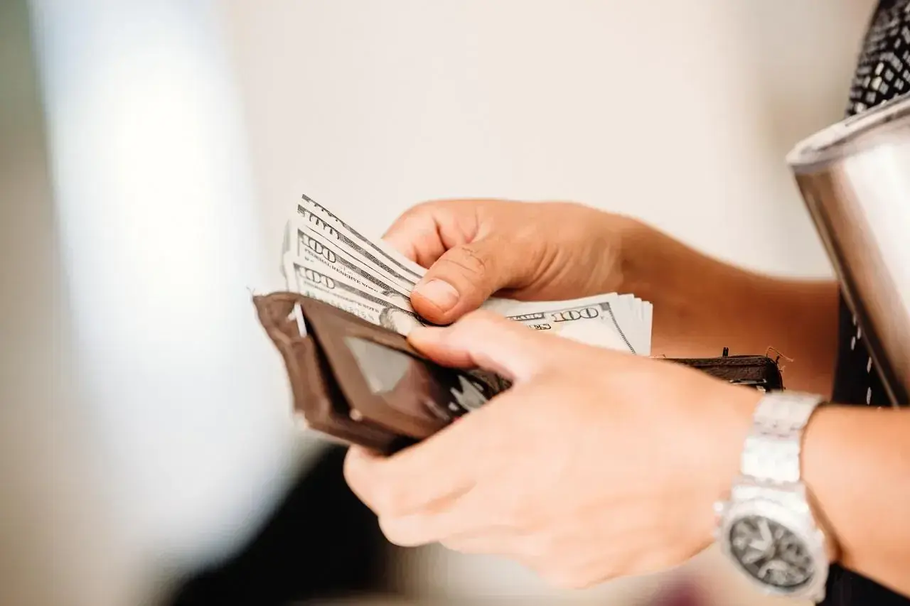 Ręce liczą banknoty 100 dolarowe, przygotowując się do wypłaty pieniędzy z Revolut.