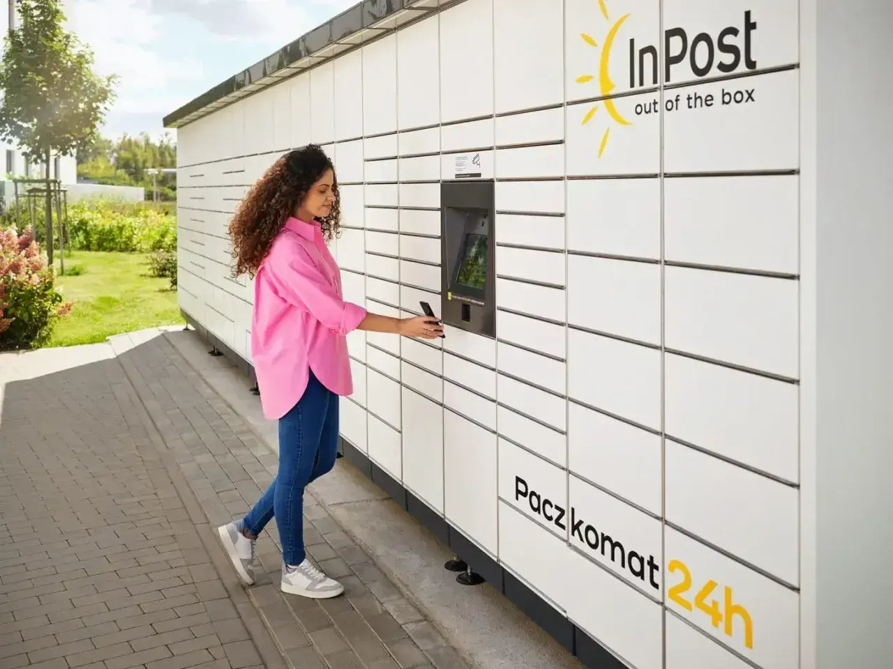 Kobieta z telefonem przy Paczkomacie InPost. Szybka wysyłka InPost za granicę to teraz norma.