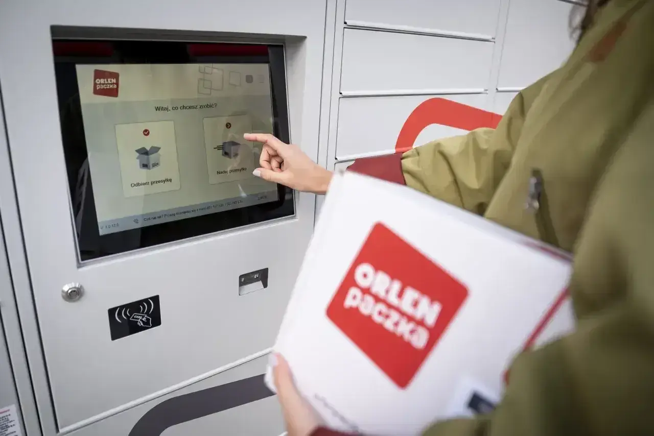 Kobieta z paczką ORLEN Paczka dotyka ekranu automatu, by nadać przesyłkę.