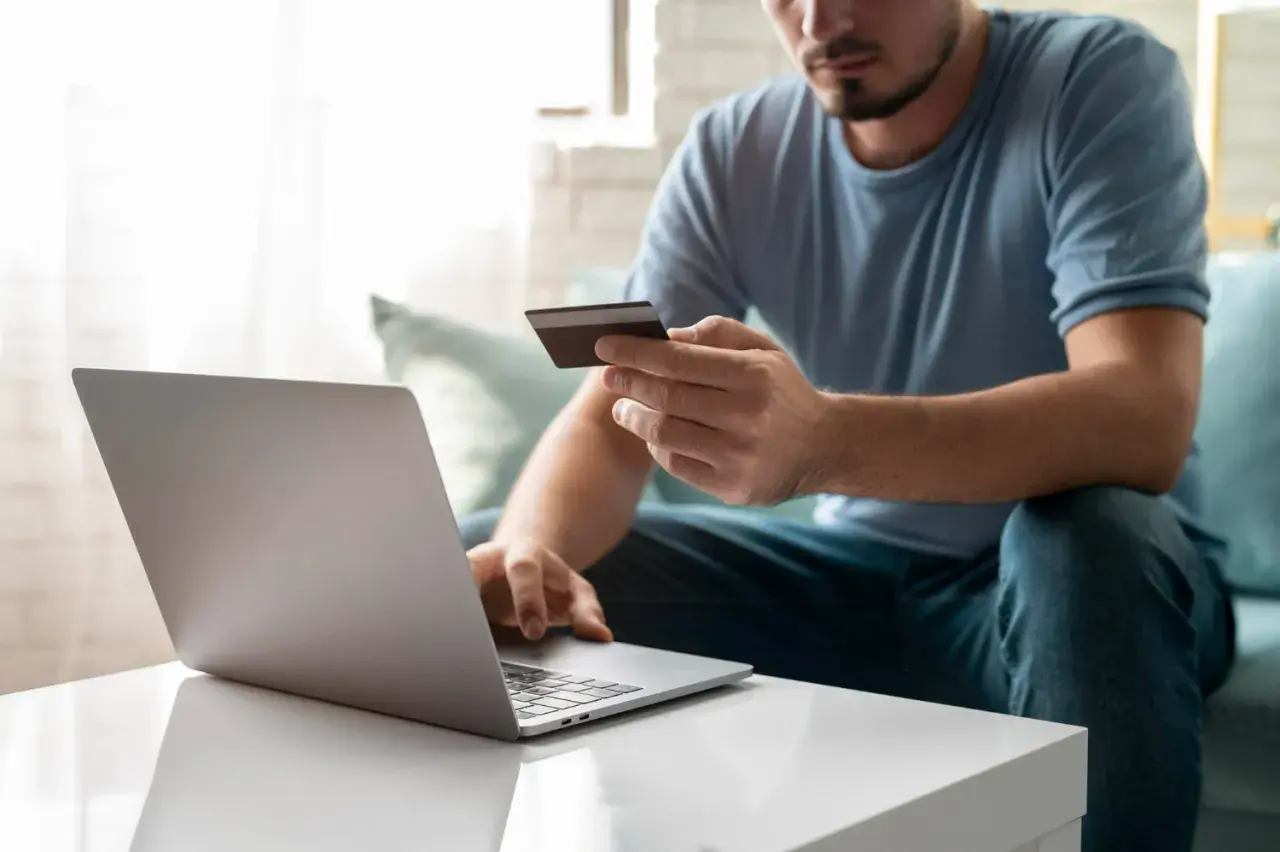 Mężczyzna z kartą kredytową przed laptopem, przygotowuje się, jak wpłacić pieniądze na PayPal.