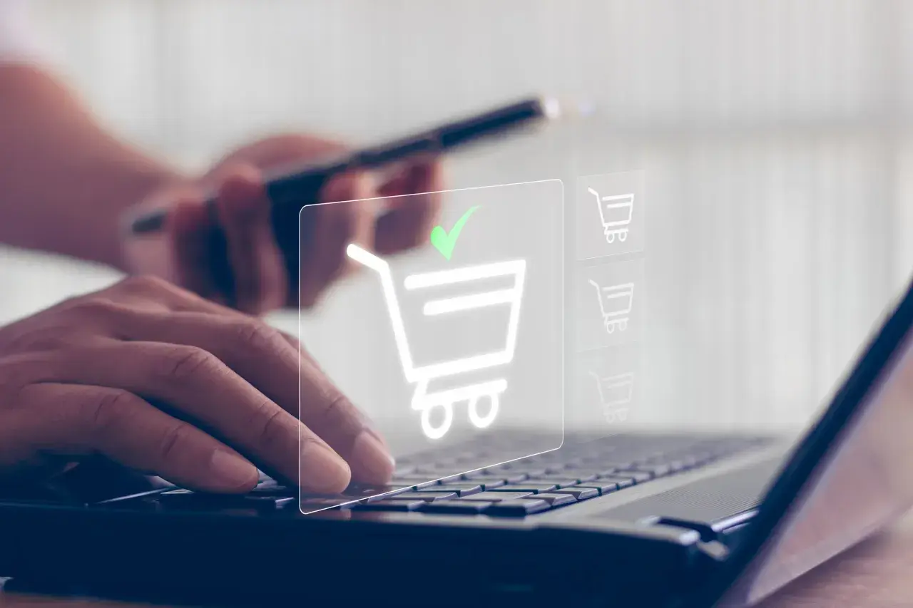 Dłonie wpisują dane na klawiaturze laptopa, a na ekranie pojawia się ikona koszyka z zielonym znacznikiem, symbolizująca udany zakup, jakby płatność przez paysafecard.