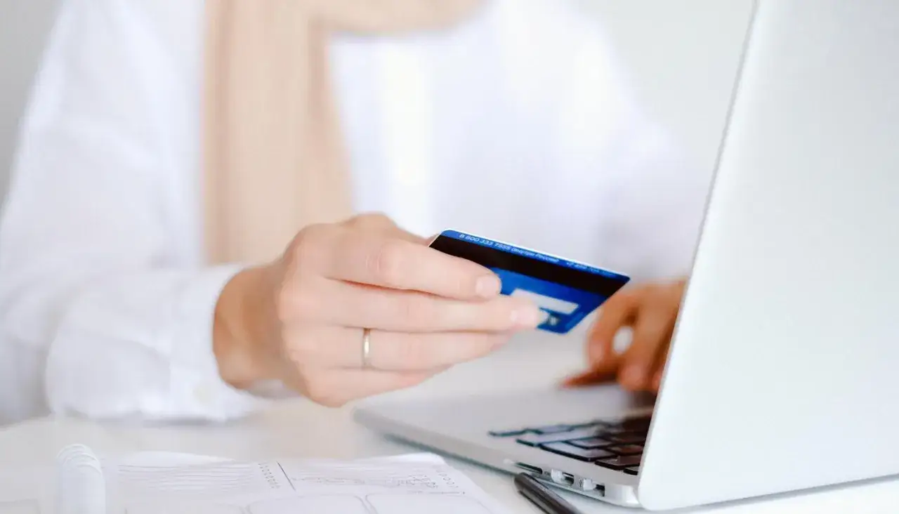 Dłoń z kartą zbliża się do laptopa, ułatwiając wygodne online payments.
