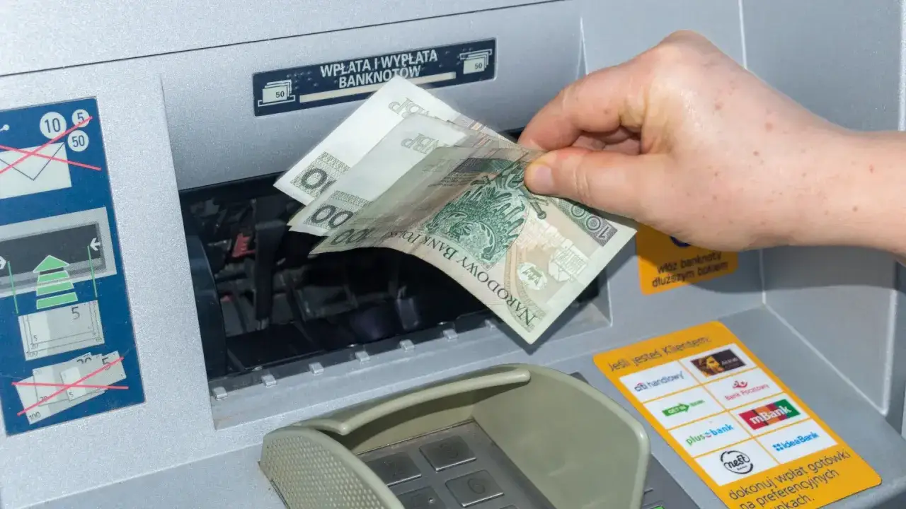 Ręka wkłada banknoty do bankomatu, pokazując, jak wyplacic pieniadze z Revolut.