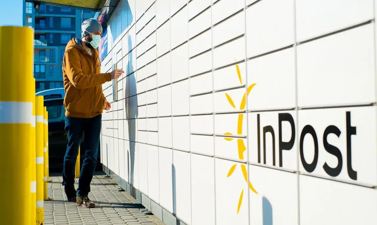 Mężczyzna w maseczce odbiera paczkę z paczkomatu InPost. To właśnie Rafał Brzoska wymyślił paczkomaty, rewolucjonizując logistykę.